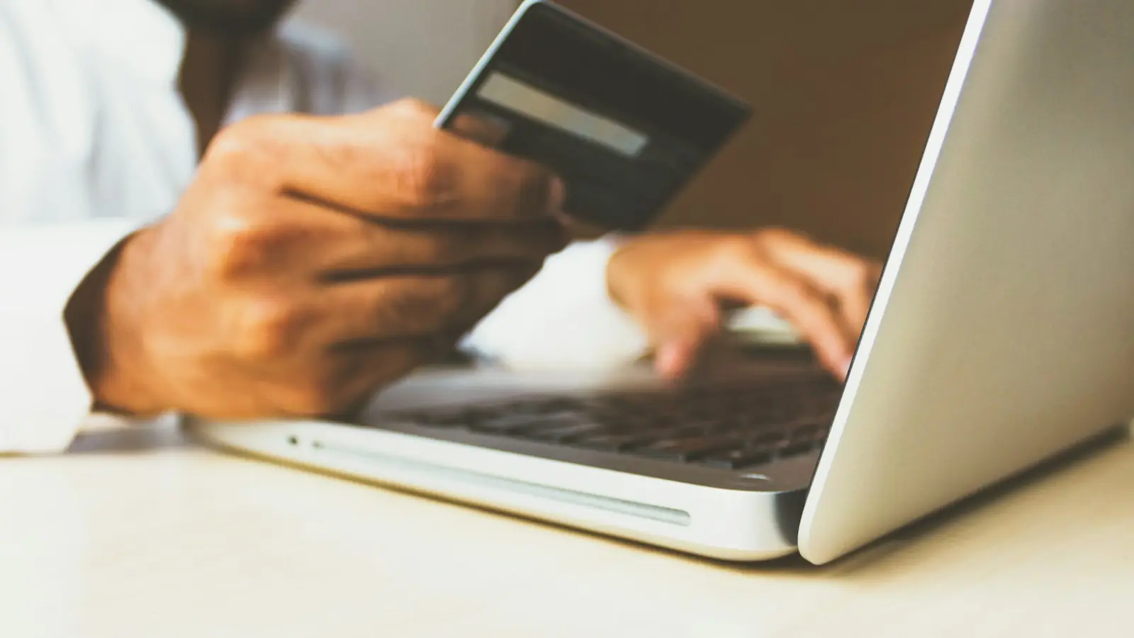Person holding a payment card in front of a laptop