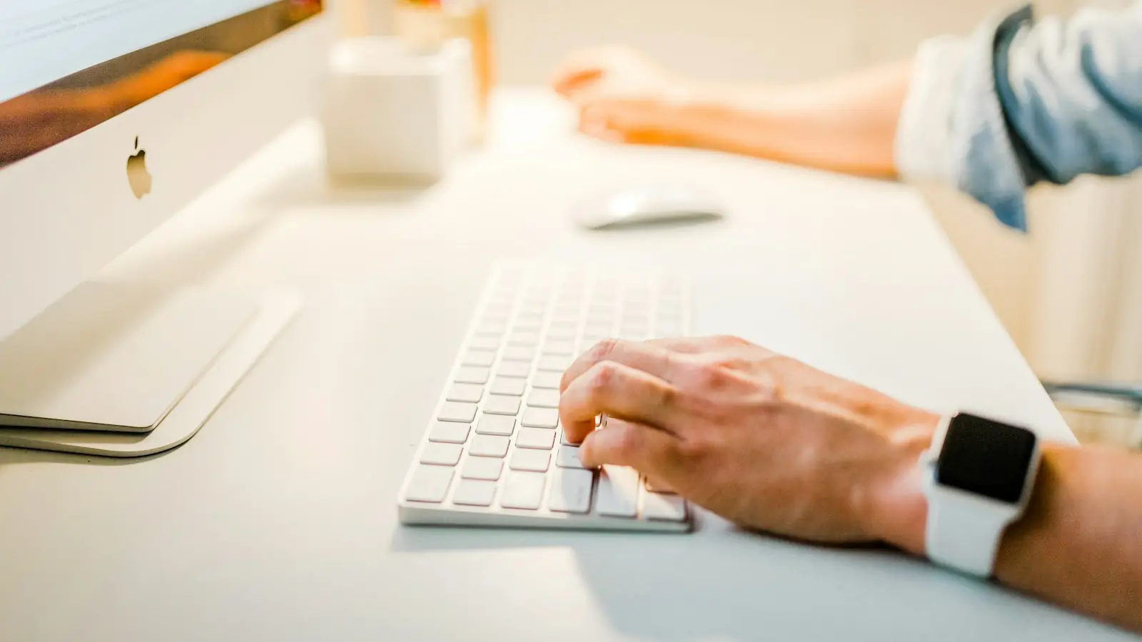 Hands typing on a keyboard next to a smartwatch